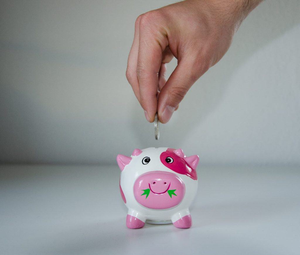 A hand putting money into a piggy bank disproving the financial myth that your business can't save money