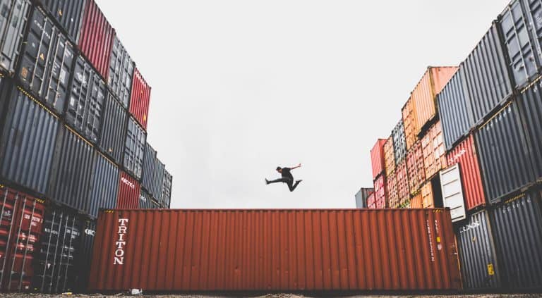 A person jumping across a shipping container in a shipping yard