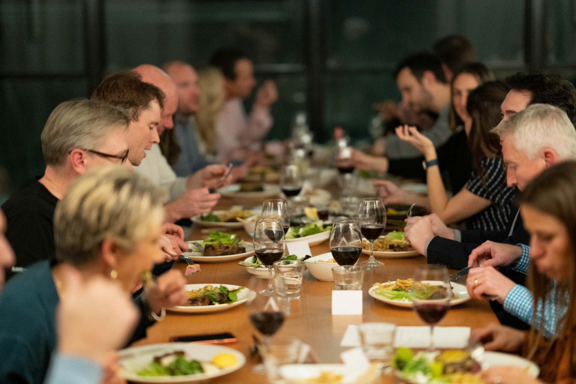 A long dinner table, full of people eating and drinking