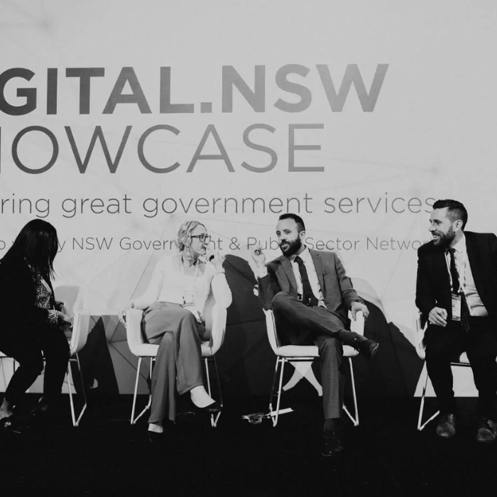 A black and white photo of PSN hosting a conference with four people on stage. They are having a conversation.