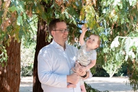 Elliott standing under some trees holding his son.