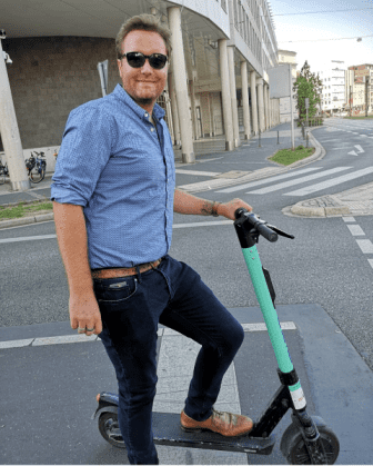 Elliott standing on a street with one foot on an electric scooter.