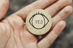 A hand holding a wooden disc with the word 'Yes' on it.