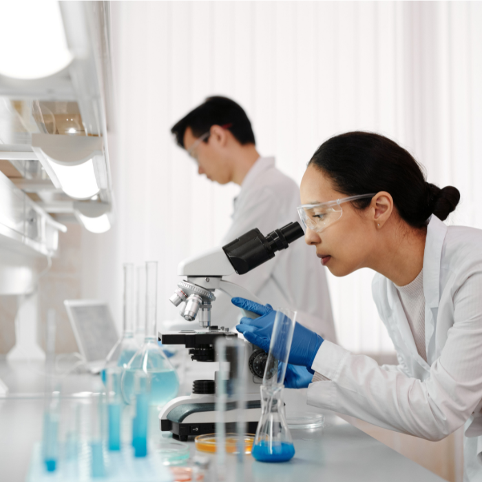 Woman in white coat looks through microscope